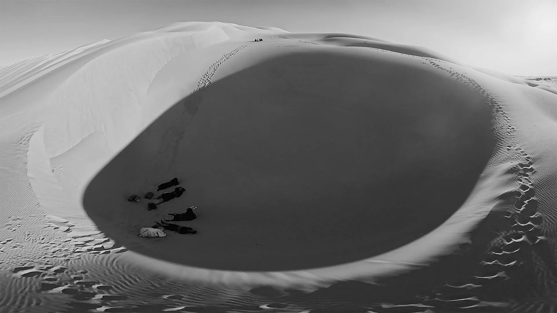 Vue plongeante sur le creux d'une dune où la famille s'est arrêtée près d'une forme enveloppée de blanc